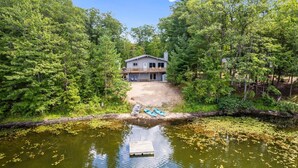 Ein Haus, umgeben von dichtem Wald, mit einem Steg, der in einen Teich führt.