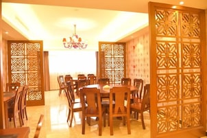 Un comedor con una mesa redonda rodeada de sillas, una araña y separadores de madera decorativos.