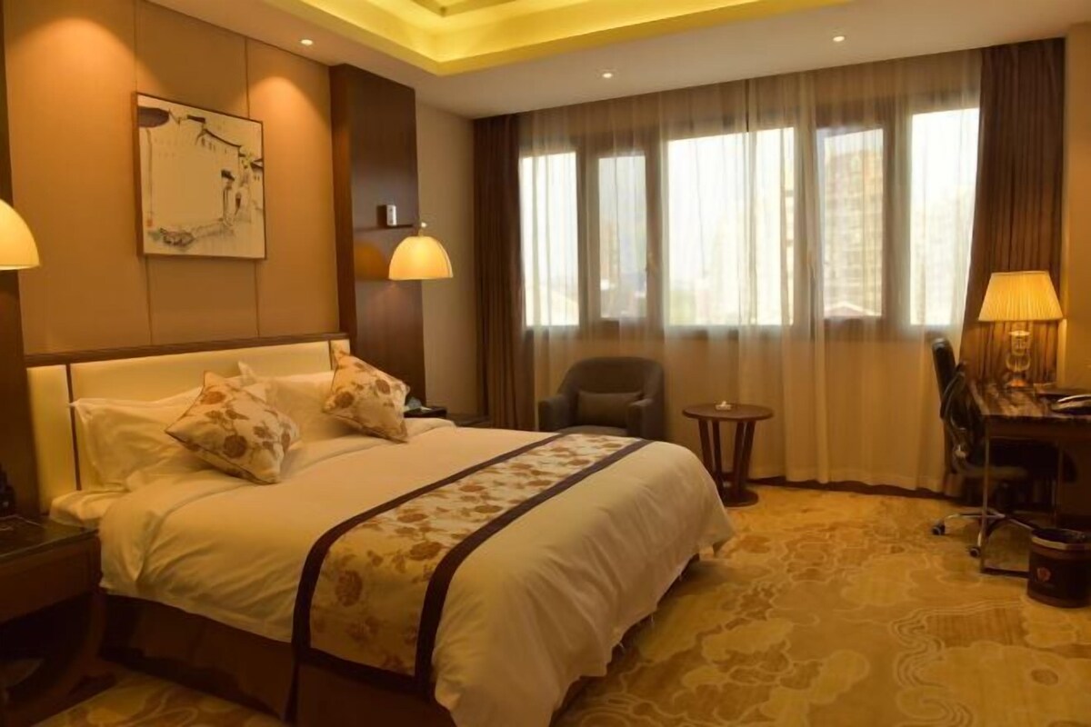 A hotel room with a large bed, a desk, a chair, and a small table.