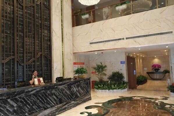 A hotel lobby with a marble reception desk, a large indoor plant, and a decorative fountain.