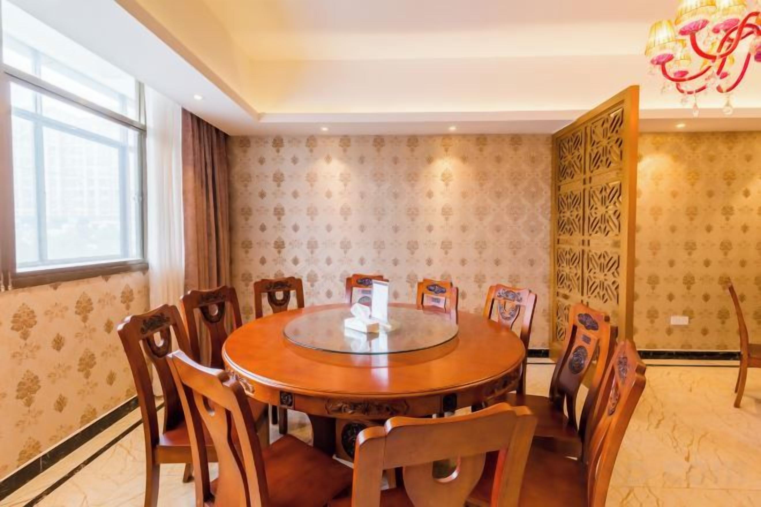 A round dining table with chairs, a chandelier, and patterned wallpaper.