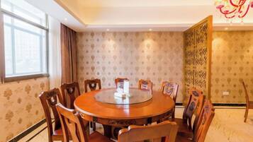 A round dining table with chairs, a chandelier, and patterned wallpaper.