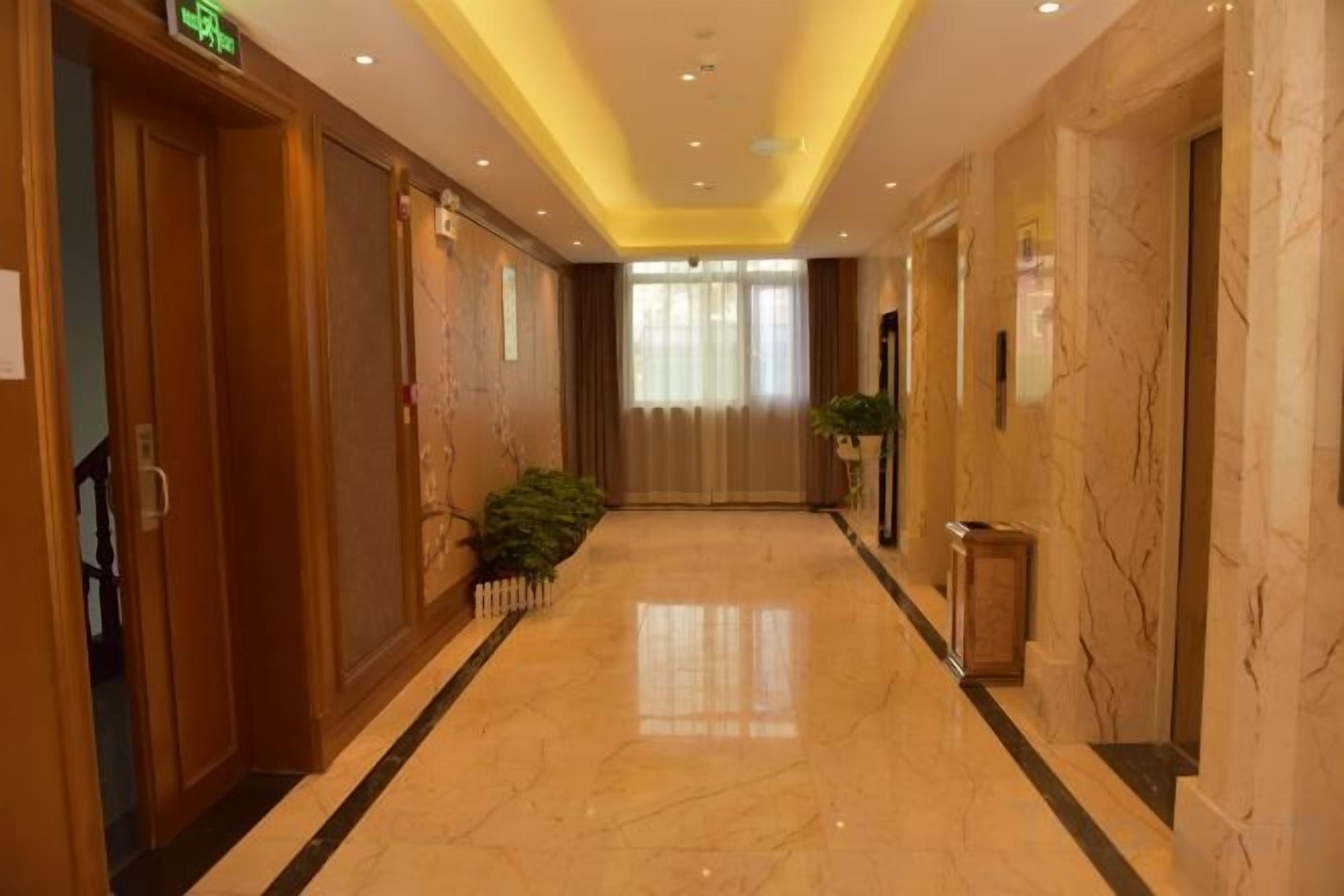 A hotel corridor with a marble floor, wooden doors, and a plant.