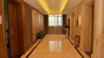 A hotel corridor with a marble floor, wooden doors, and a plant.