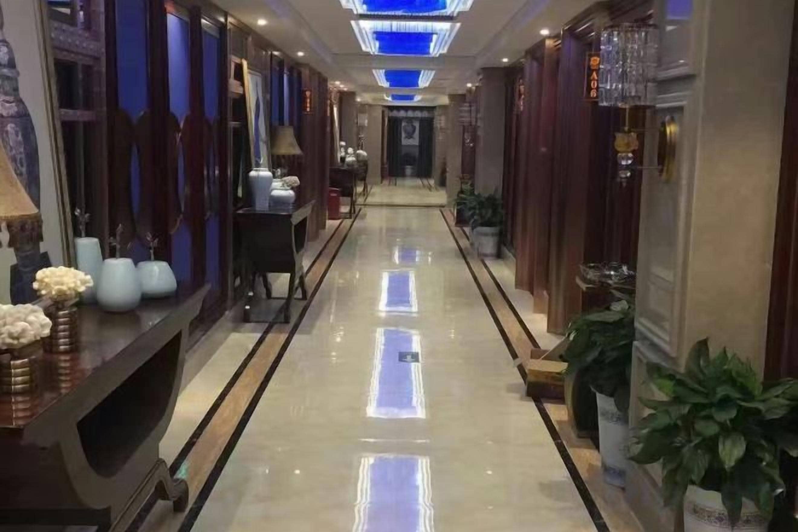 A hotel corridor with a reflective floor, potted plants, and a reception desk.