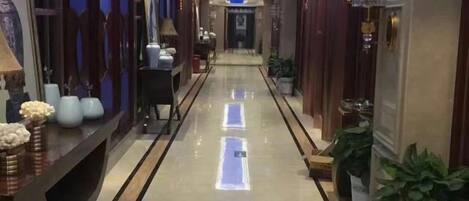 A hotel corridor with a reflective floor, potted plants, and a reception desk.