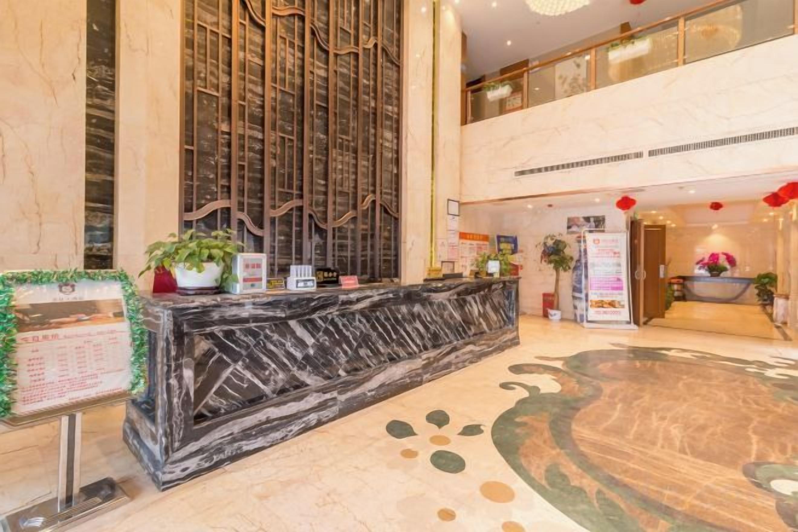 A hotel lobby with a reception desk, a vertical decorative panel, and a large circular carpet.