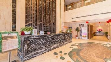 A hotel lobby with a reception desk, a vertical decorative panel, and a large circular carpet.