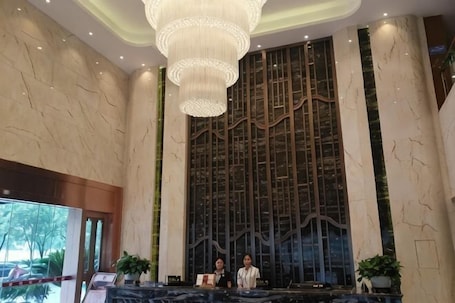 A lobby with a reception desk, a large chandelier, and a wall with vertical lines.. Mingshi Hotel
