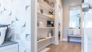 Ein modernes Interieur mit einer Wand in geometrischem Muster, einer Holzbänkl mit Kissen und einer eingebauten Regalwand mit Dekorationselementen.