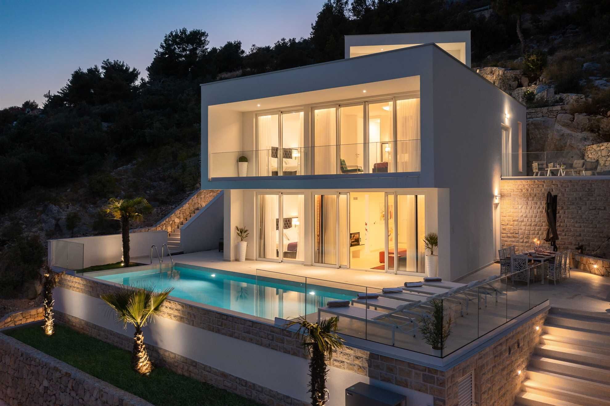 A modern two-story house with a swimming pool, stone walls, and a balcony overlooking the pool.