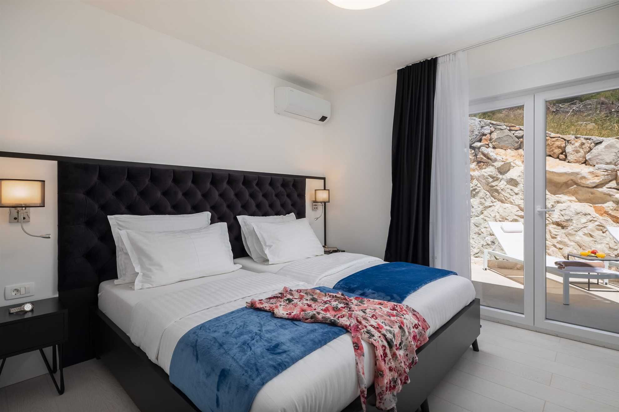 A hotel room with a large bed, two bedside tables, a wall-mounted air conditioner, and a view of the outdoors.