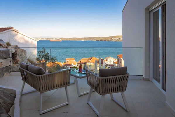 A balcony with two wicker chairs, a small table, and a view of the sea and buildings. - Adria View Villas Complex (Seget Donji)