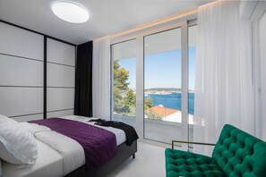 Een slaapkamer met een groot raam, een bed, een groene stoel en uitzicht op zee.