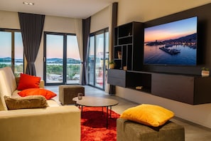 Un salon moderne doté d’un grand téléviseur, de sièges confortables et offrant une vue sur une étendue d’eau.