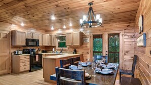 A wooden cabin interior with a kitchen, dining area, and a sign reading "The Cabin is my Happy Place".