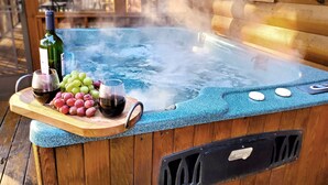 A hot tub with steam rising, surrounded by wooden deck and a wooden cabin in the background.