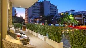 An outdoor seating area with wicker furniture and potted plants, overlooking a cityscape at dusk. - Loft 268 "Beautiful Modern Condominium" in  Romantic Zone, Puerto Vallarta. (Puerto Vallarta)