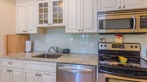 A kitchen with white cabinets, a stainless steel sink, a microwave, a stove, and a dishwasher. - One Bedroom Deck Villa Steps from Duval! (Key West)
