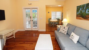 A living room with a sofa, a coffee table, and a dining area with a table and chairs. - One Bedroom Deck Villa Steps from Duval! (Key West)