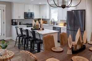 Une cuisine moderne avec des meubles blancs, un réfrigérateur en acier inoxydable et un coin repas comprenant des chaises en bois et un îlot central.