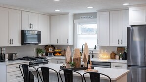 Una cocina moderna con armarios blancos, un refrigerador de acero inoxidable, horno empotrado y una isla grande con taburetes de bar.