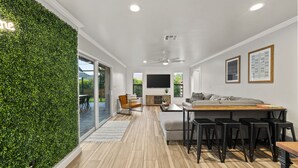 A modern living room with a green wall, wooden flooring, a sofa, a coffee table, and a TV. - NEW Naples Modern Farmhouse w/Heated Pool, Sleep 10 (Naples)