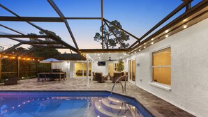 A pool area with a glass enclosure, outdoor furniture, and a pergola with string lights. - NEW Naples Modern Farmhouse w/Heated Pool, Sleep 10 (Naples)
