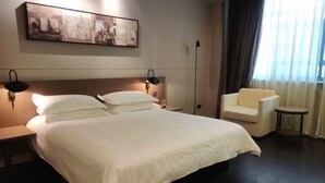 A hotel room with a large bed, two bedside tables, a chair, a small table, and a painting on the wall. - Jinjiang Inn Select (Taixing Runtai South Road) (Taixing)