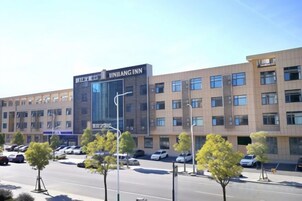 Un edificio de hotel con un letrero claro, varios pisos y un estacionamiento lleno de coches.