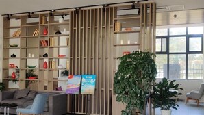 A modern reception area with a wooden bookshelf, a large potted plant, and a grey sofa. - Jinjiang Inn Select (Taixing Runtai South Road) (Taixing)