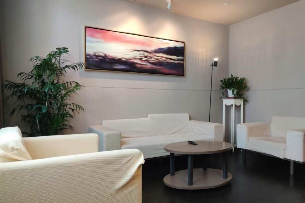 Ein modernes Wohnzimmer mit einem weißen Sofagarnitur, einem runden Couchtisch und einem großen abstrakten Gemälde an der Wand.