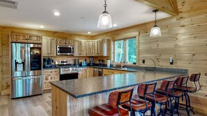 A modern kitchen with wooden cabinetry, stainless steel appliances, and a central island with bar stools. - Gorgeous dog-friendly cabin with great view, deck, hot tub, & gas fireplace (Kingfield)