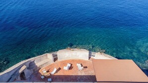Vue aérienne d’une propriété située sur la côte, dotée d’une terrasse et d’un espace extérieur aménagé avec des sièges, le tout offrant une vue sur la mer.