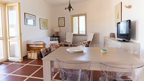 Une pièce comprenant une table à manger, des chaises, un canapé, un téléviseur et des tableaux encadrés accrochés aux murs.