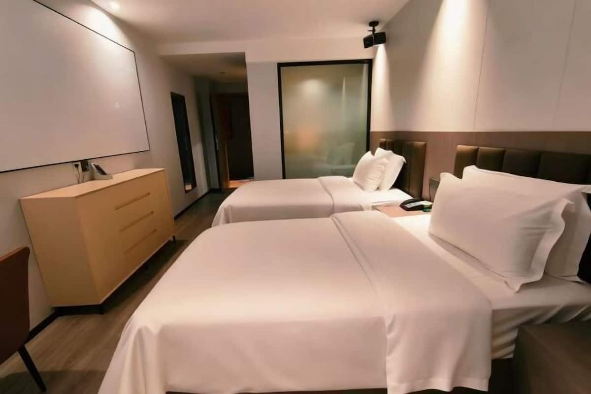 A hotel room with two beds, a bedside table, a dresser, a mirror, and a sliding door.