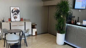 A reception area with a reception desk, a potted plant, and a framed artwork on the wall. - Laiyueke Hotel (Shenzhen)