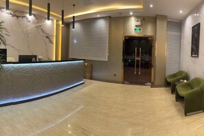 A reception area with a marble wall, a reception desk, green chairs, and a glass door leading to a room.