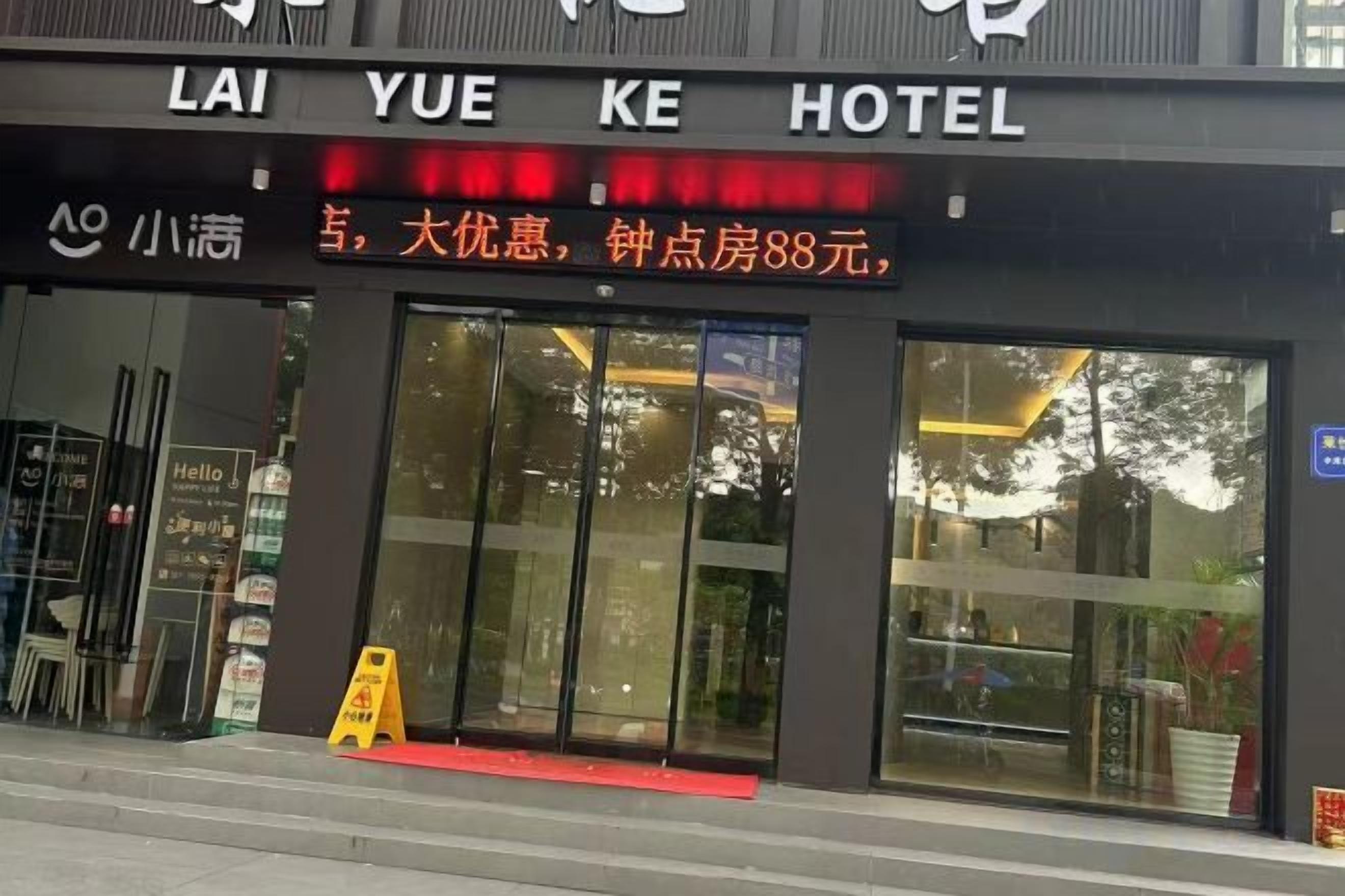 A hotel entrance with a large glass facade, a red carpet leading inside, and a signboard with text.