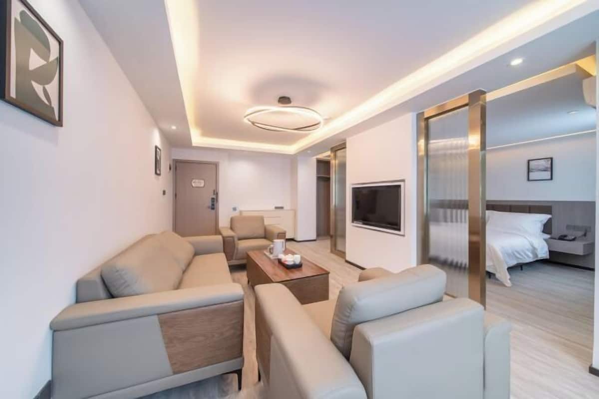 A modern hotel room with a sofa set, a coffee table, a TV, and a bed with a headboard.