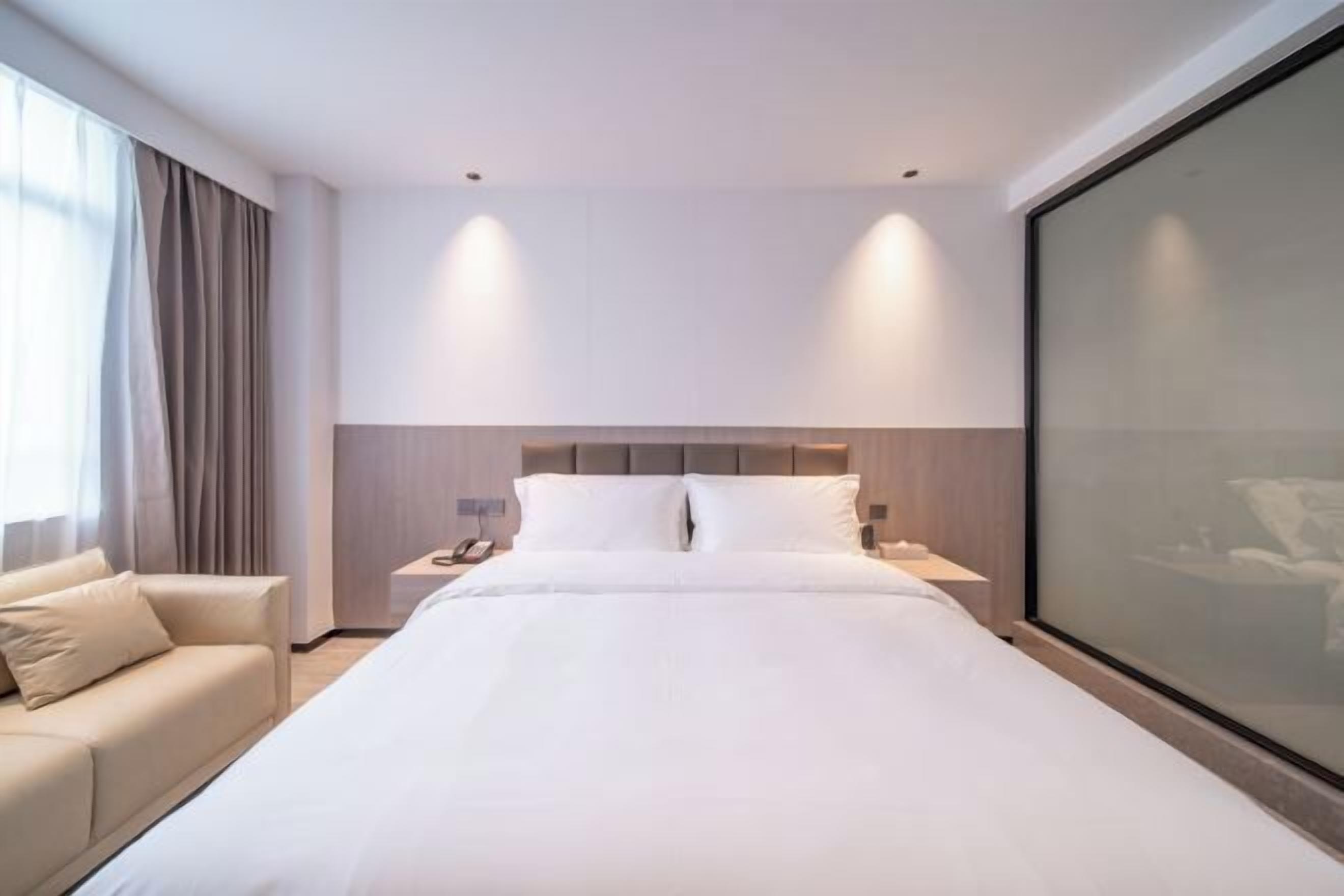 Habitación de hotel con una cama grande, dos mesitas de noche, un sofá y un ventanal con cortinas.