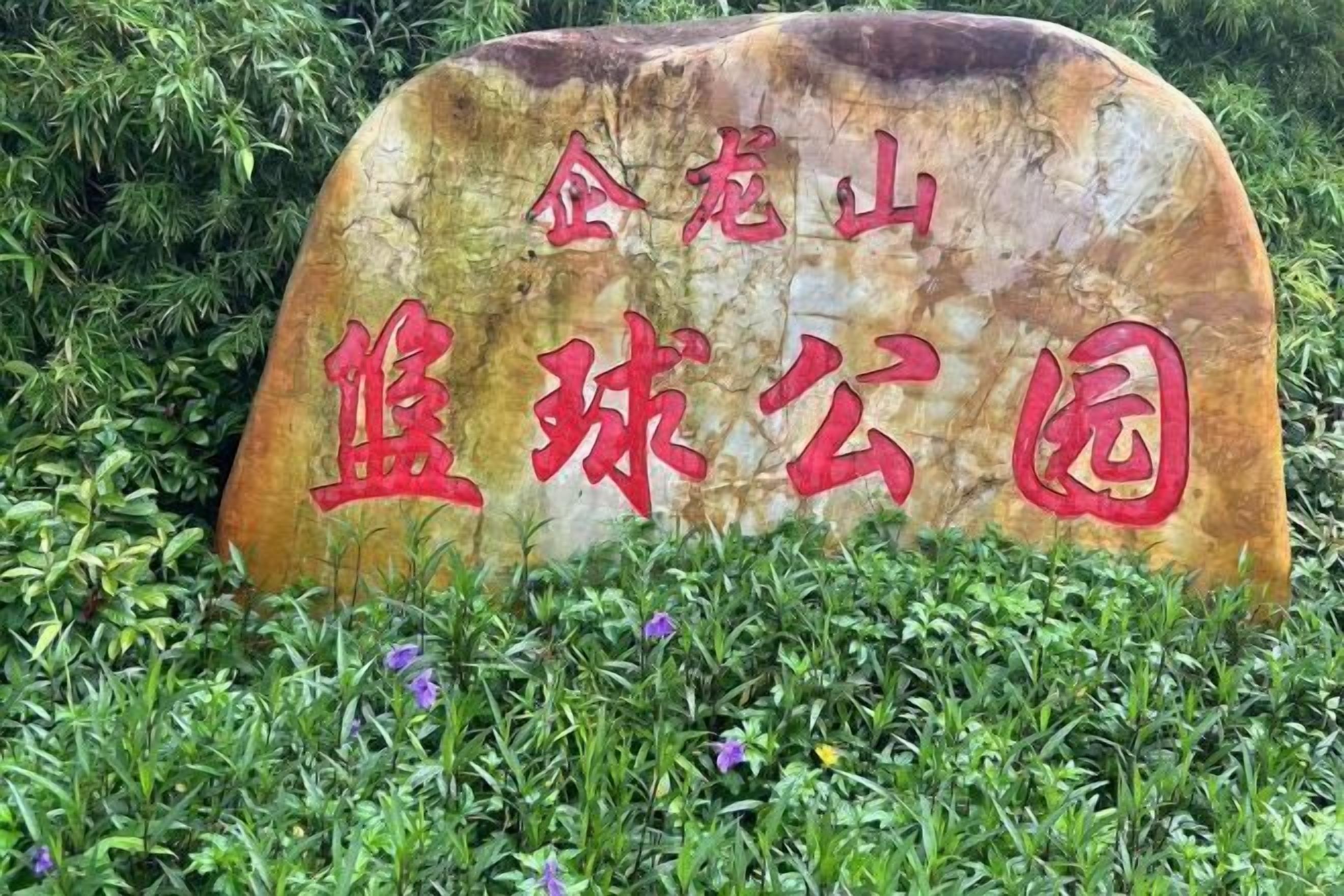 A stone sign with red Chinese characters surrounded by greenery.