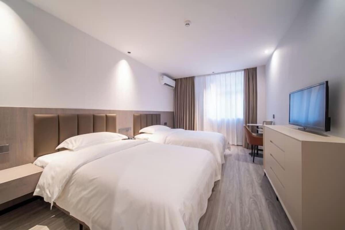 A hotel room with two beds, a desk, a television, and a window with curtains.