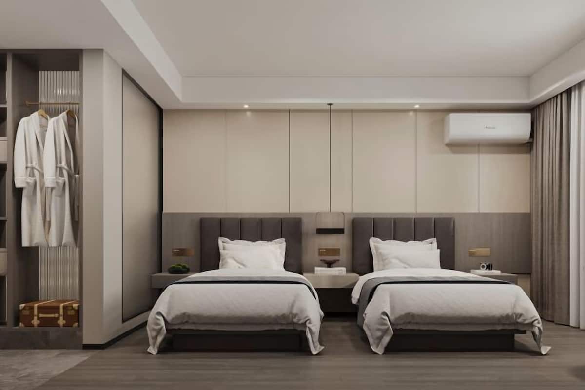 A modern hotel room with two beds, a wardrobe, and an air conditioning unit.