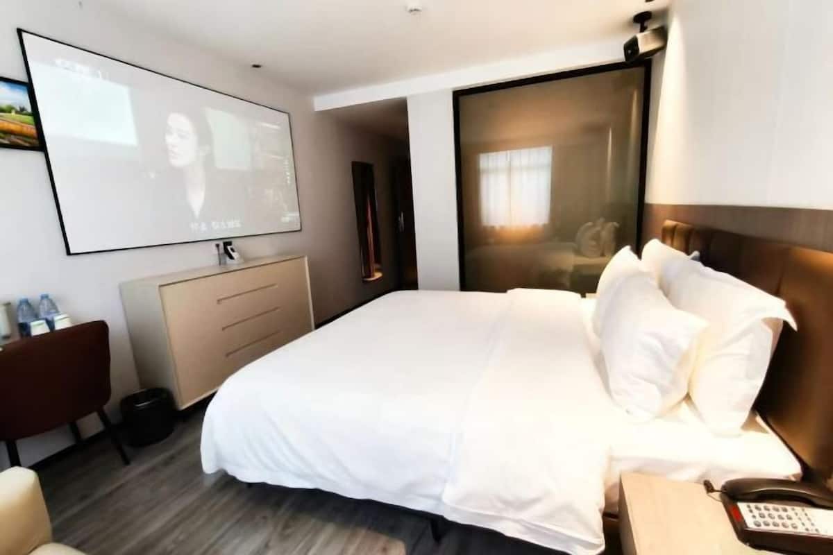 A hotel room with a bed, a desk, a phone, and a TV screen.
