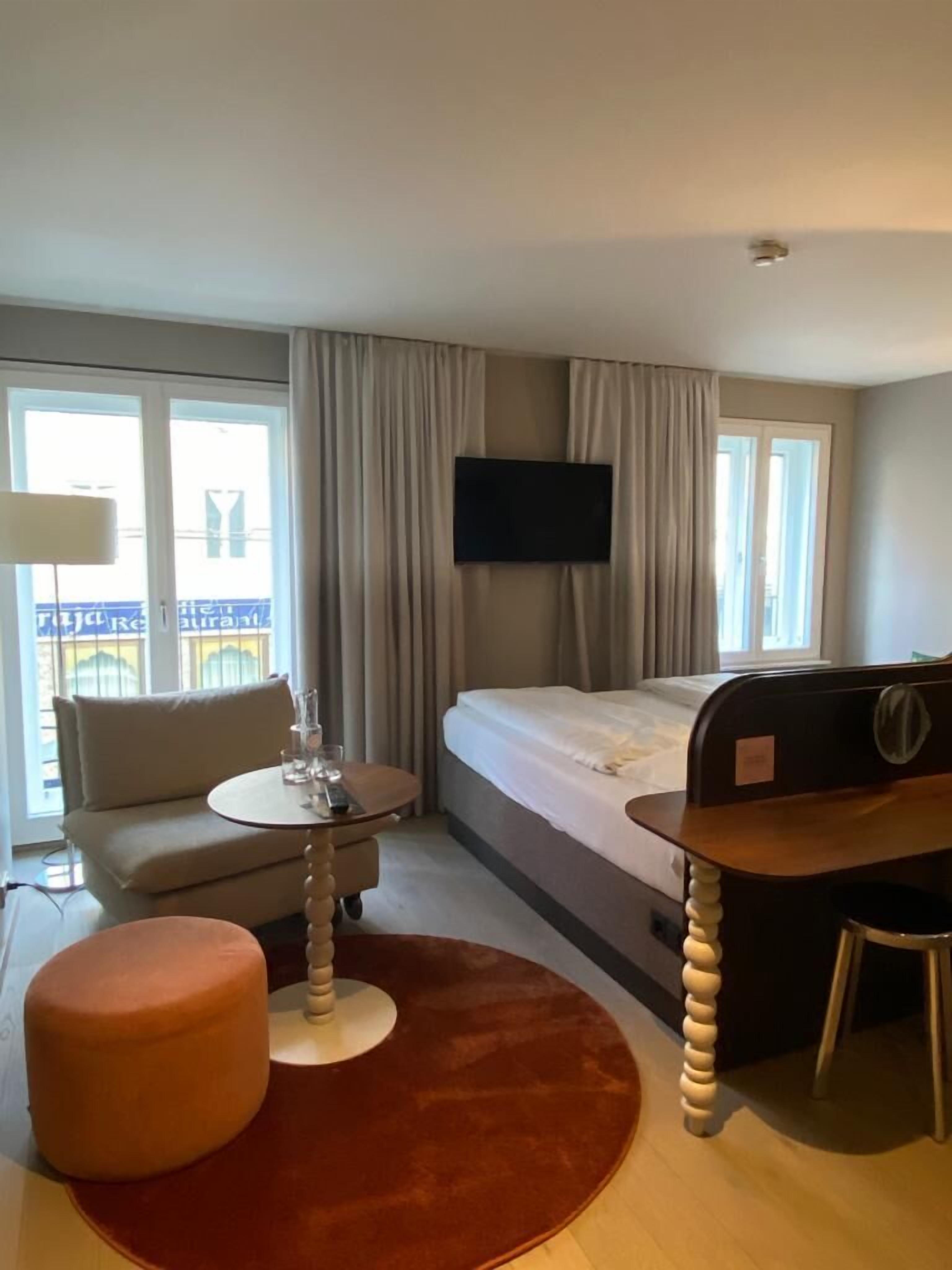 Ein Hotelzimmer mit einem Bett, einem Schreibtisch, einem Stuhl, einem Sofa, einem kleinen Tisch und einem Fernseher.