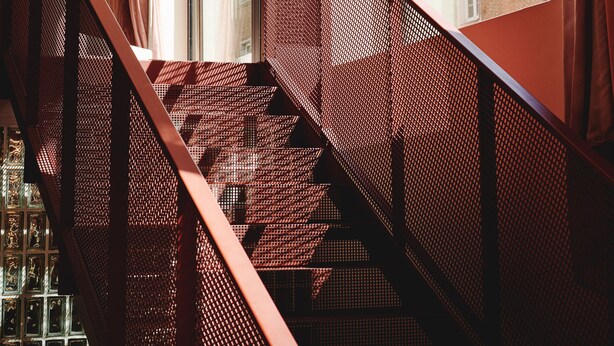 Eine Treppe mit Metallgeländer und einem Fenster, in dem ein Schild mit der Aufschrift 'Café Tagesbar by MUS' zu sehen ist.