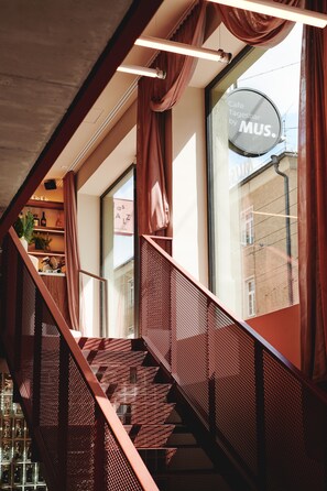 A staircase with a metal railing and a window with a sign reading "Café Tagesbar by MUS."