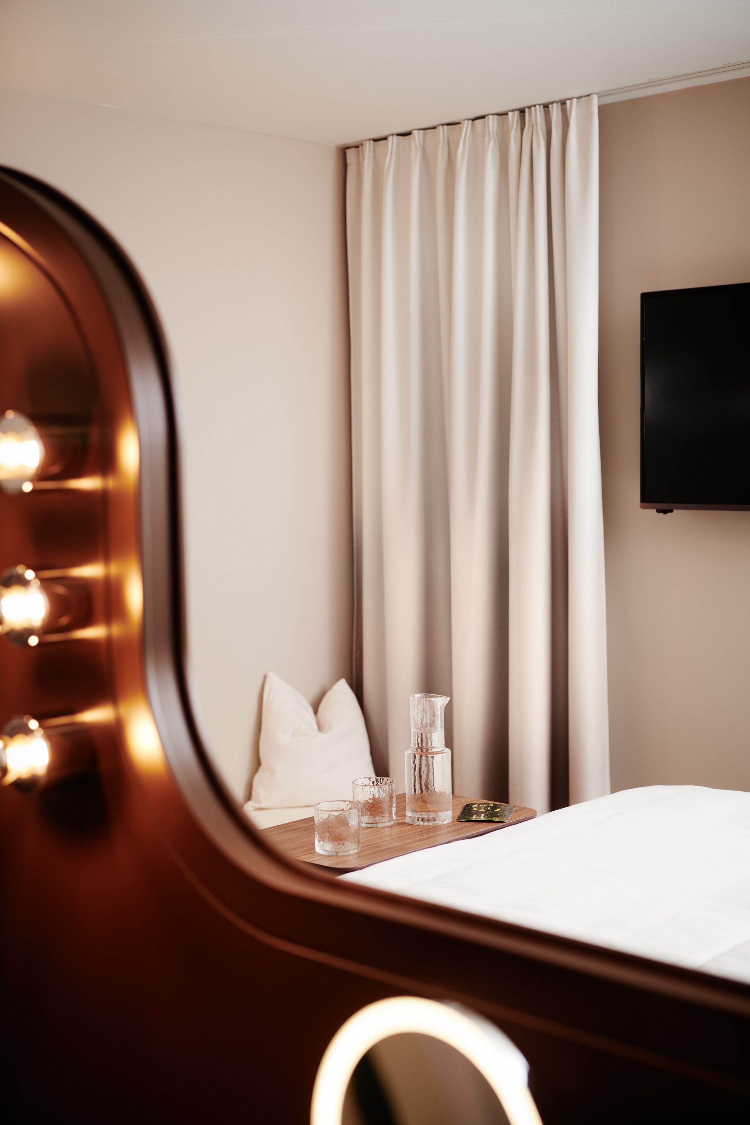 Ein Hotelzimmer mit Bett, Schminkspiegel, Flachbildfernseher und einem Fenster mit Vorhängen.