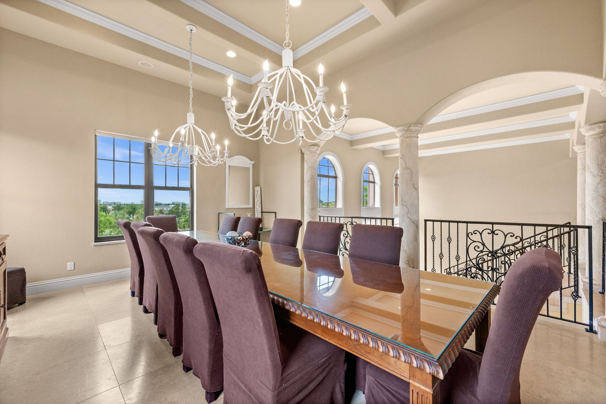 A spacious dining area with a large glass table, multiple chairs, and elegant chandeliers.